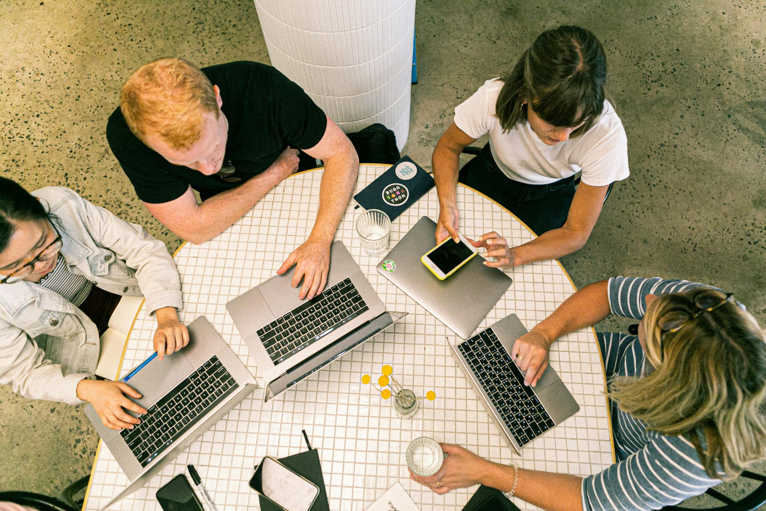 Aerial view of 4 people working on 3 x laptops and a phone.