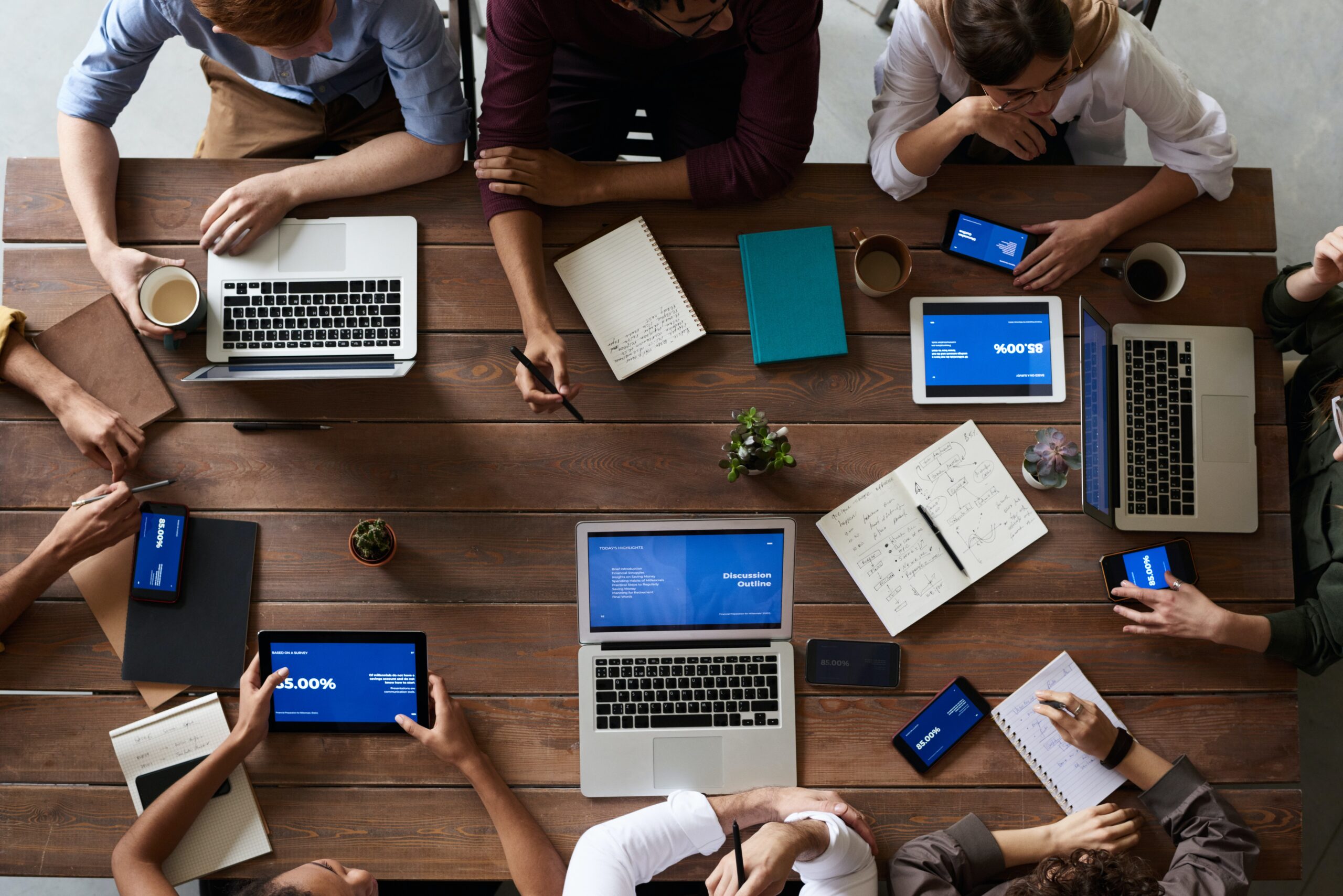 Aerial view of desk with 8 people attending a meeting with various technologies