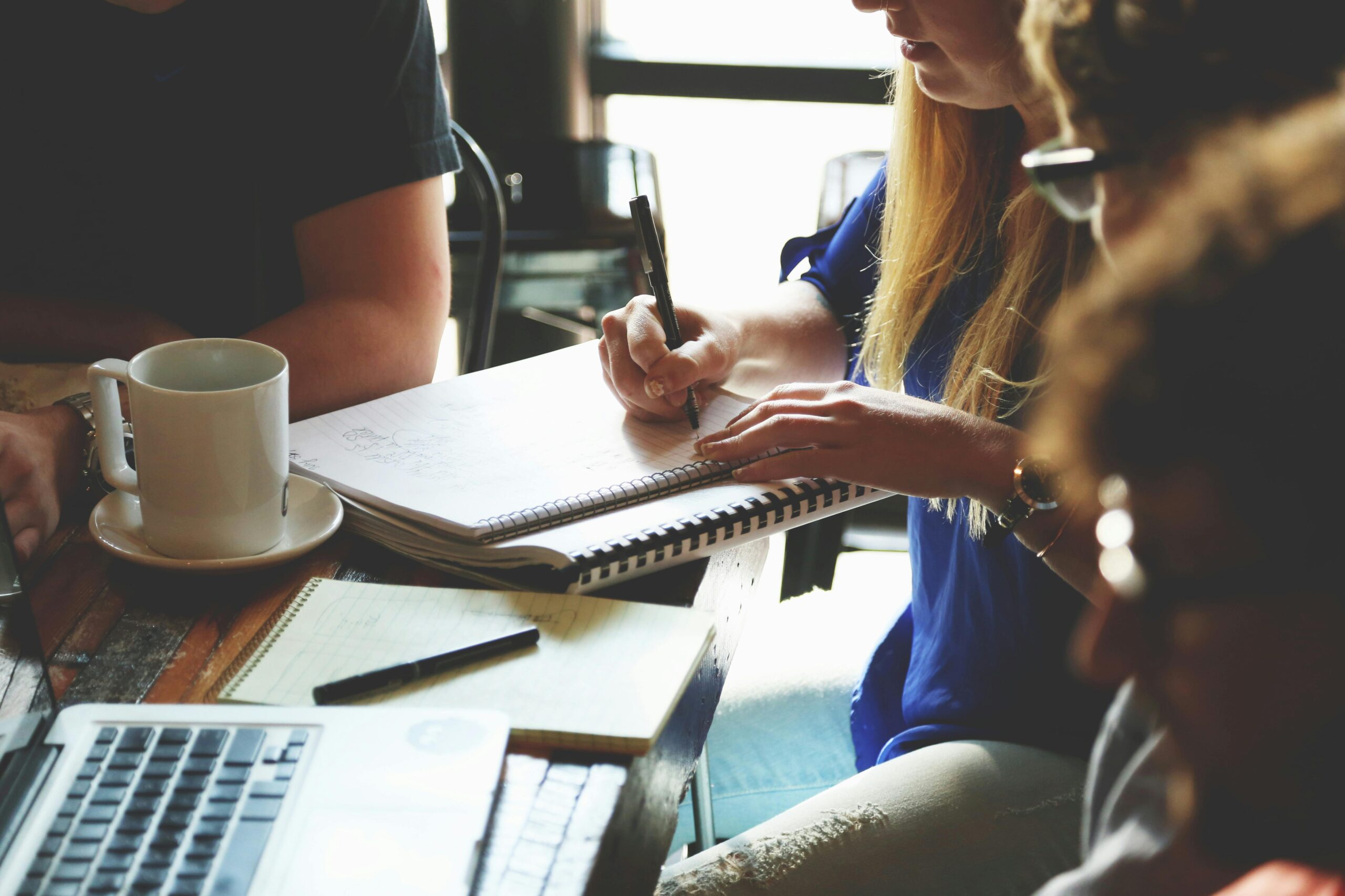 A group meeting setting, where someone is writing notes in a notebook.